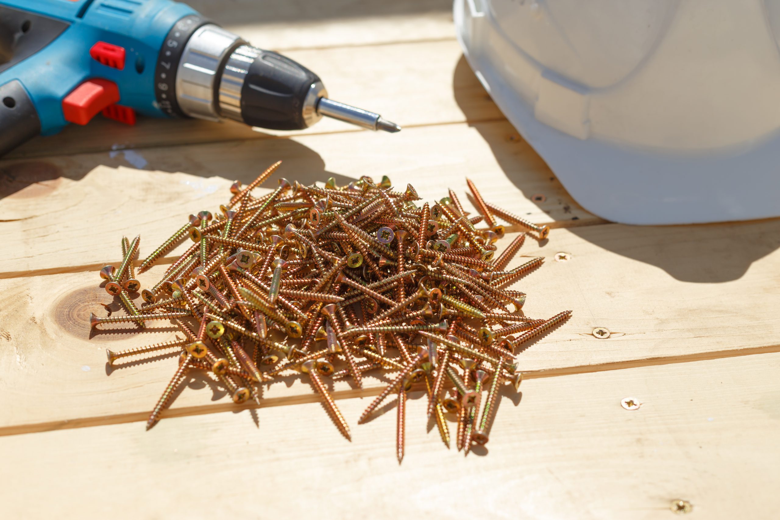 Tools for the construction of a wooden floor or terrace. Screwdriver, self-tapping screws and helmet on the wooden floor. View from above.